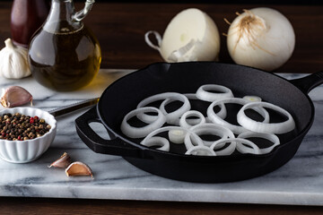 Close up of a fry pan filled with white onion slices ready for cooking.