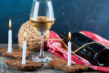 A glass of white wine and bottle with burning candles, close up
