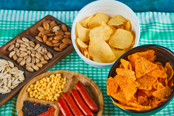 Assorted snacks, bowl of chips and a plate of sausages on a blue table