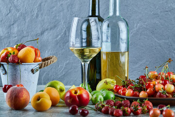 Two bottle and glass of wine on marble table with bunch of summer fresh fruits