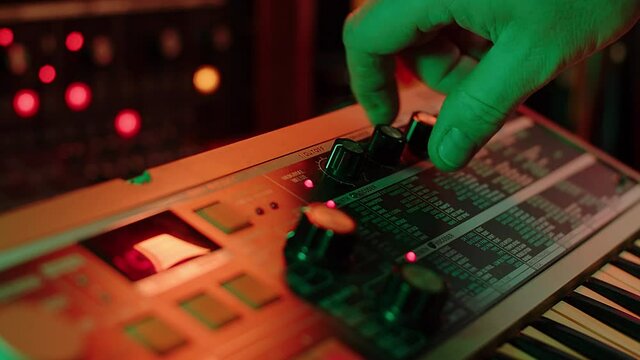slow motion shot of a man playing keys and changing settings on a vintage synth, red and green mood