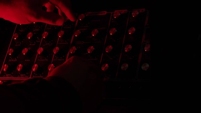 slow motion shot, close up, man turnig knobs on vintage synth during live show, dark mood