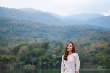 Portrait image of a beautiful young asian woman standing in front of the lake and mountains