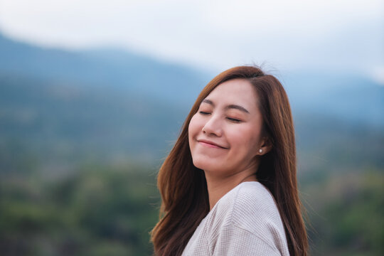 Portrait image of a beautiful young asian woman close her eyes while standing in front of the mountains outdoors