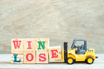Toy forklift hold letter block e to complete word win lose on wood background