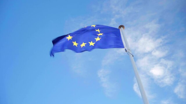 Looking up the EU flag waving on its own in strong wind on a blue and cloudy sky, symbol of the European Union alliance