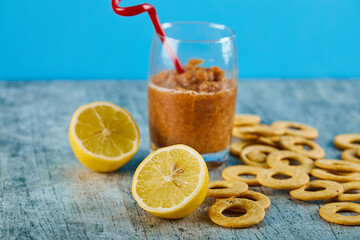 A glass of juice with straw, lemons and crackers on gray table