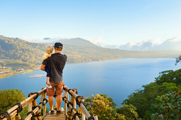 Summer family vacation. Young father with baby son stand at balcony on high cliff. Happy child look at amazing tropical jungle view. Buyan lake is popular travel destinations in Bali island, Indonesia