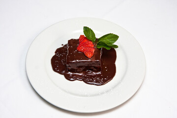Chocolate cake with strawberry, icing sugar and melted chocolate, red berries served on white plate on white background