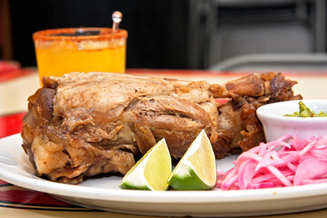 Plate of pork knuckle with lemons, red onion, guacamole and drink, close up view