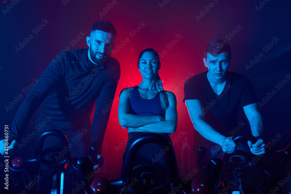 Wall mural sportive people standing behind the bike in gym and looking at camera posing, in tracksuits