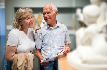 Positive elderly man and woman with guidebook standing at hall of Art Museum