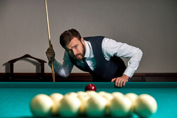 Fototapeta premium man playing billiard or snooker with concentration and serious face looking at balls on table, sport game concept