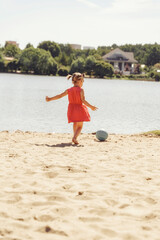 Little cute girl plays in ball on the beach. Summertime concept.