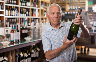 Older man looking for perfect wine for solemn occasion in wine store..