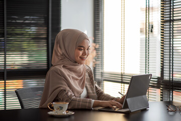 Fototapeta na wymiar Beautiful Asian Muslim woman working on tablet in office, smiling face.