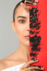 Beautiful young woman and poster with mascara strokes against grey background