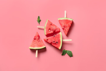 Slices of ripe watermelon with wooden sticks on color background
