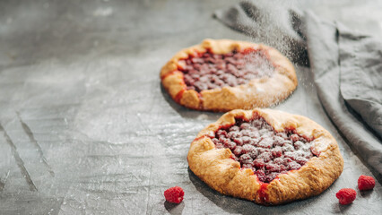 Raspberry galette with copy space. Powdered sugar poured onto delicious rustic homemade tart with frozen or fresh raspberries on gray background