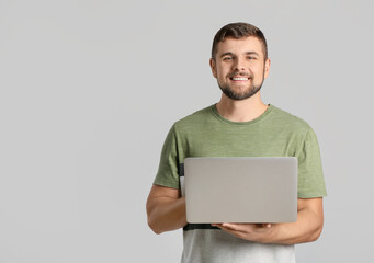 Young man with laptop on light background