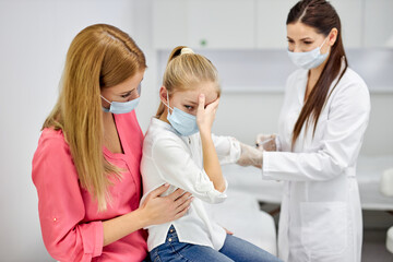 female doctor taking blood sample test of a little girl in the clinic, frightened girl sits with mother, woman technician making blood tests on child in the laboratory of blood extractions