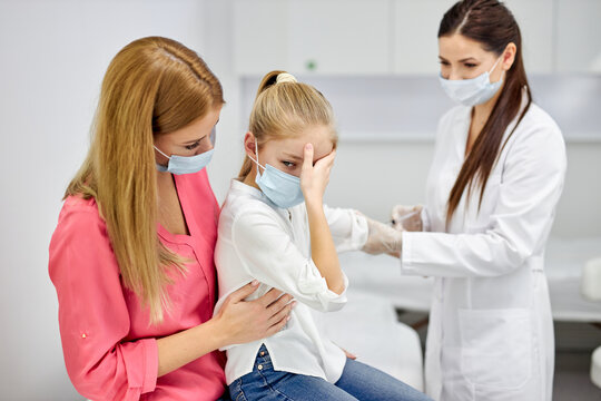 female doctor taking blood sample test of a little girl in the clinic, frightened girl sits with mother, woman technician making blood tests on child in the laboratory of blood extractions