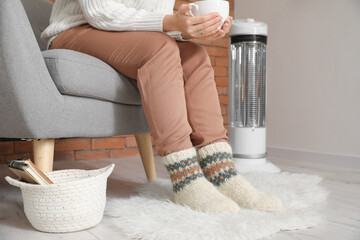 Young woman in warm clothes and cup of tea at home. Concept of heating season