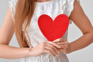 Young woman with red heart on grey background, closeup