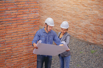 Structural engineer and architect working with blueprints discuss at the wall building structure, outdoor construction site.