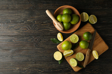 Bowl and board with lime on wooden background, space for text