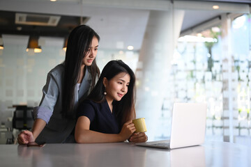 Happy friendly employee talking to her colleague teammate sharing ideas chatting at office.