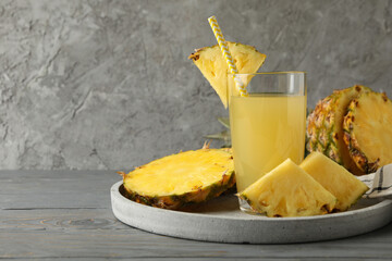 Tray with pineapple slices and glass of juice on wooden table, space for text