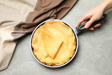 Female hand hold pan with thin pancakes on gray table