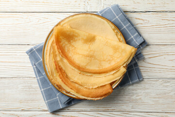 Kitchen towel with plate of thin pancakes on wooden background