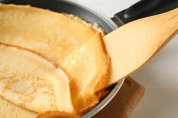 Pan with tasty thin pancakes and spatula on wooden table