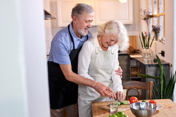 elderly couple carving vegetables together, handsomegray haired man help wife to cook