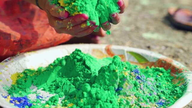 Close up of kid hands taking colorful holi powder from plate during festival celebrations