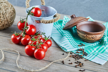 Bucket of tomatoes and cloves on wooden table with empty bowl