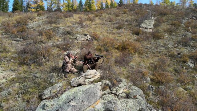 hunters with rifles are waiting for the beast on the rock, one aims at the beast, the second lures, flying back, Republic of Tuva, Russia