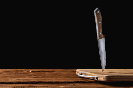An old vintage metal knife stuck in a wooden cutting board on a table. Horizontal view. Isolated on black background with copy space for text. Mock up