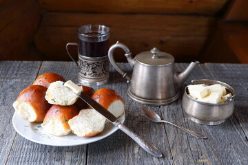 Tasty buns on a white plate are surrounded by silver utensils on gray wooden table.