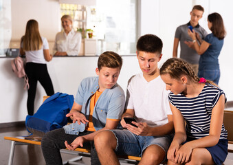 Fototapeta premium Group of three teenage schoolmates with smartphones on break in college