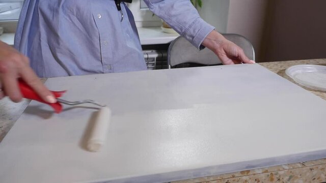Closeup of female hand painting the kitchen frame in white with roller brush