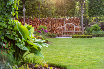 Obraz premium Zielony trawnik z drewnianą ławką w ogrodzie w angielskim stylu