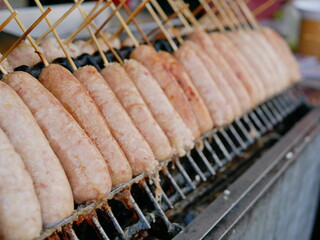 Selective focus of rice and pork sausage on sticks being cooked on a hot grill / stove - street food in Thailand