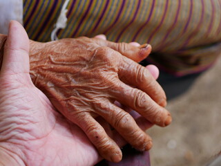 Fototapeta premium Hands of an old hard working woman on a hand of a younger man - care for elderly people