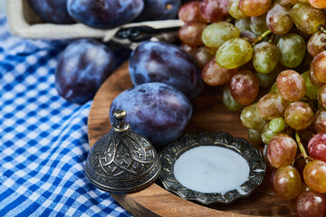 Fresh plums and a bunch of grapes on a wooden plate