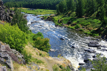 The mountain river flows among the green banks