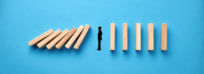 Silhouette of a businessman in apathy or inertia against collapsing wooden dominos on blue...