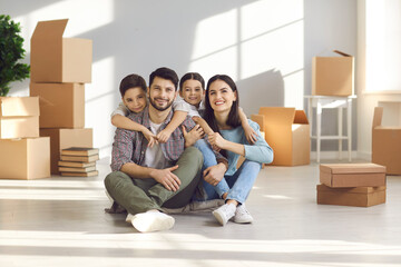 Portrait of a happy family sitting on the floor between cardboard boxes in their new apartment. Husband and wife and their child moving in new home. Concept of buying your own home and moving.